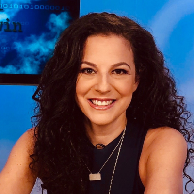 White woman with curly brown hair in front of a blue background