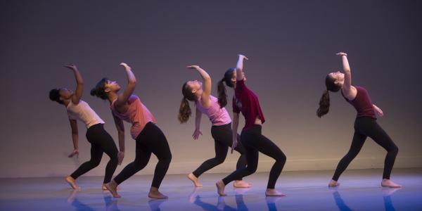five women on stage in a backward-leaning dance position