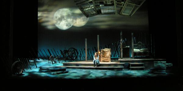 Young woman sitting alone on a stage, set design by Rob Morgan