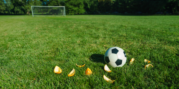 A soccer ball in a field surrounded by 9 orange slices with 8 eaten