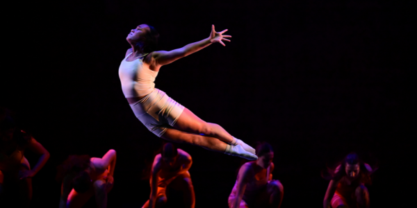 A dancer leaps through the air with arms spread