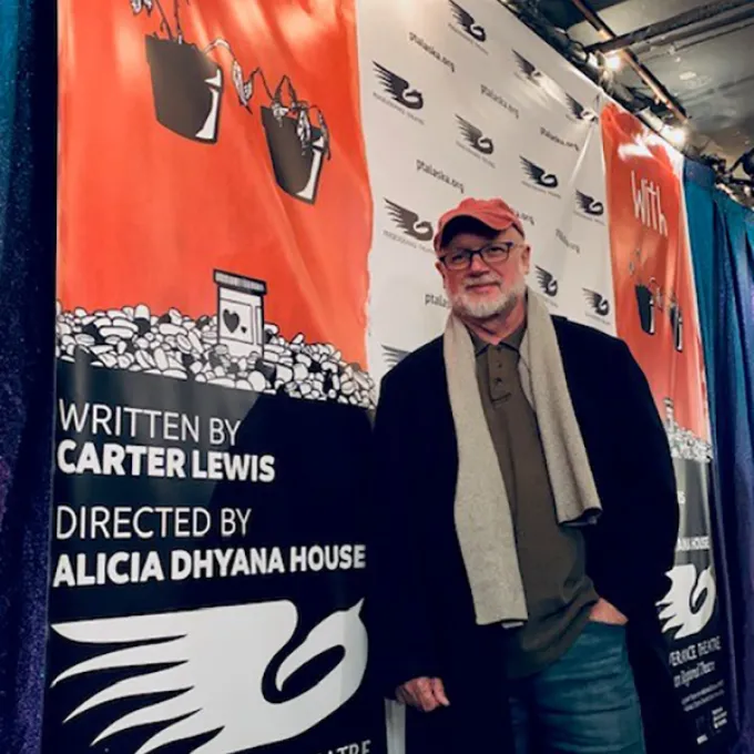 Photo of Carter Lewis in front of the show poster for the play "With".